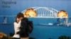 Пара цілується перед картиною, на якій зображено Керченський міст у вогні під час нападу Росії на Україну, у центрі Києва, 8 жовтня 2022 року